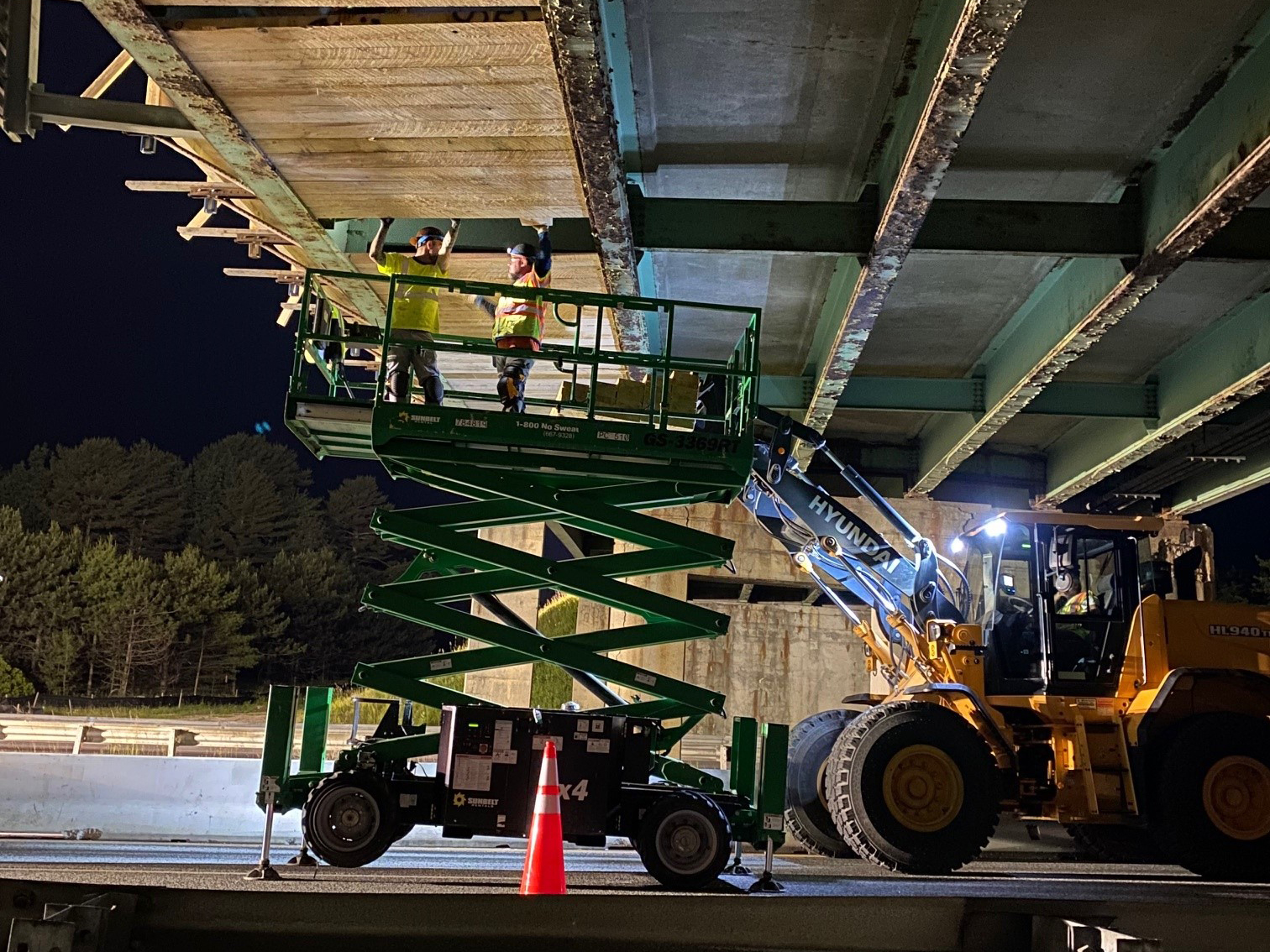 Workers in a scissor lift truck install shielding on the underside of the bridge.